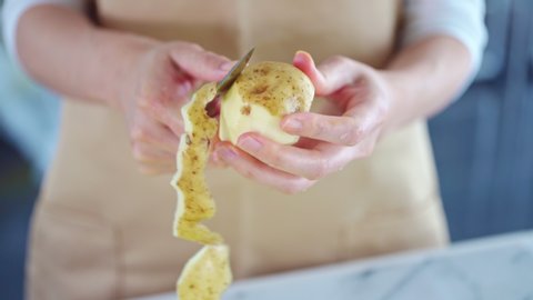 People peelings a potato skin in kitchen.