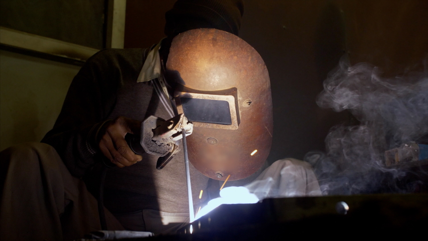 A worker welding at the metal factory in India. 4K stock footage of a worker with a protective mask welding metal at a workshop | Shutterstock HD Video #1038067664