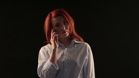 beautiful red-haired girl in a white shirt talking on a smartphone isolated on a black background. Phone advertising. Businesswoman in work