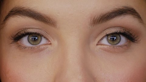 Young woman looks straight into the frame and closes her eyes slow motion. Beautiful girl with green brown eyes close-up
