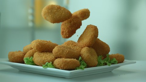 Appetizing tasty yellow chicken nuggets fall into the breakfast plate. The concept of nutritious high-calorie food. Harmful and fatty foods. Slow motion