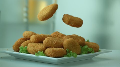 Appetizing delicious breaded chicken nuggets on falling on a plate with a green lettuce for breakfast. The concept of a delicious lunch and a charge of satiety for the whole day. Slow motion