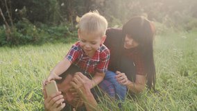 happy family teamwork outdoors have fun concept outdoors slow motion lifestyle video . mom dad and son take a photo with a smartphone in nature are sitting on the grass have fun playing .mom girl dad