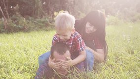 happy family teamwork outdoors have fun concept outdoors slow motion video. mom dad and son take a photo with a smartphone in nature are sitting on the grass have fun playing. mom girl lifestyle dad