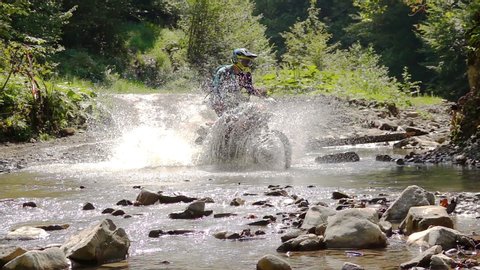 Enduro Motocycle Rider Crosses Mountain River Splashes of Water and Dirt. Slow Motion.