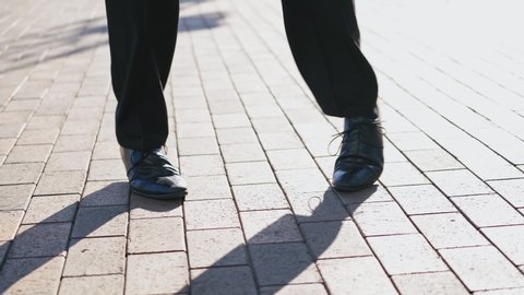 Close-up for legs of man in black shoes dancing in the street. Male's feet in black shoes and trousers dances happily on the pavement outdoors.