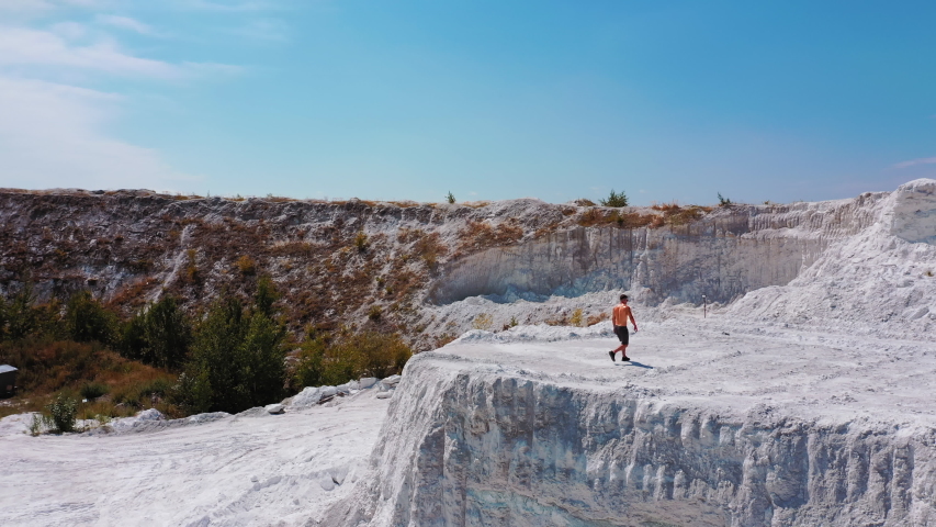 Aerial view on white canyon and a sportsman outdoors. Young athlete walking on beautiful white hill on the natural background in summer. Shirtless athlete in shorts under blue sky.