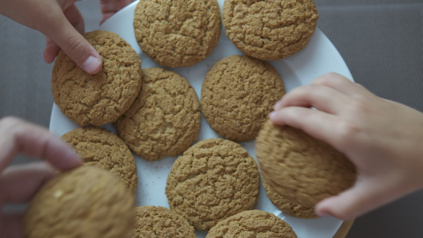 Eat oatmeal cookies. A view of a plate full of oatmeal cookies. Many hands take one by one cookies from the plate. | Shutterstock HD Video #1038130790