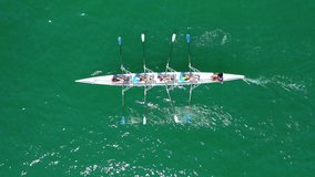 Aerial drone top down video of sport canoe operated by team of young men in emerald clear and calm lake waters