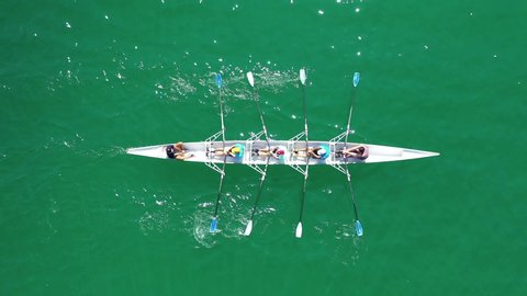 Aerial top down video of sport canoe operated by team of young men in emerald clear and calm lake waters