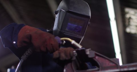 4K Female welder in metal workshop lifting up visor & smiling. Slow motion.