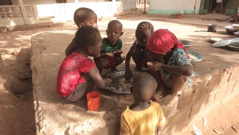 Jarra Region, The Gambia, Africa, May 30, 2018: wide angle video of a group of kids eating ramadan meal - pasta and chicken, from a silver basin, outdoors on a sunny day