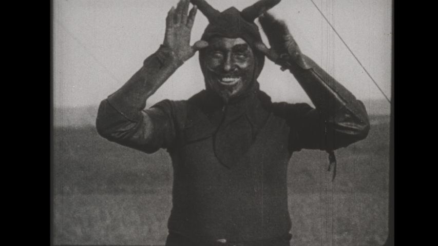 1920s A Man in a Devil Costume Ignites Smoke Bombs, Climbs a Ladder and Zip Lines with Trailing Smoke, This Daredevil Goofs for the Camera after his Stunt is Complete. 