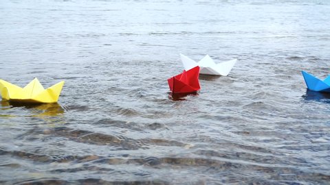 Four multicolored paper boats sailing on water on romantic sunset. Origami. Slow motion