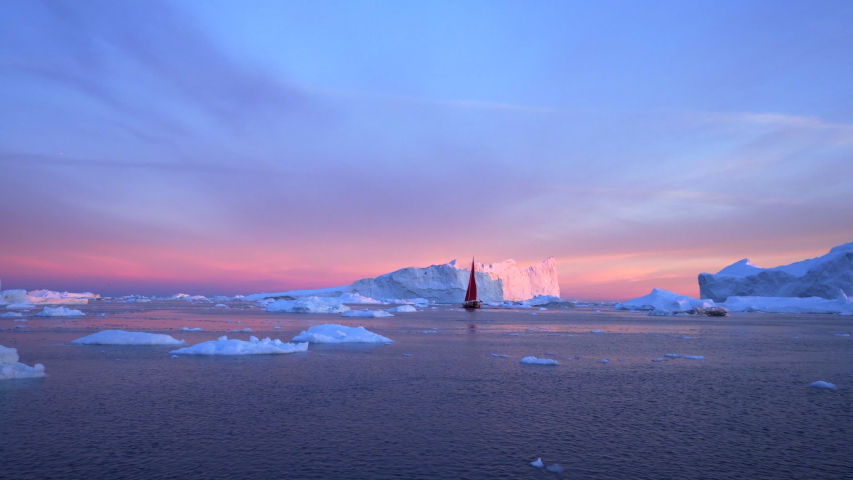 Red sailboat near floating icebergs during sunset - Disko Bay, Greenland