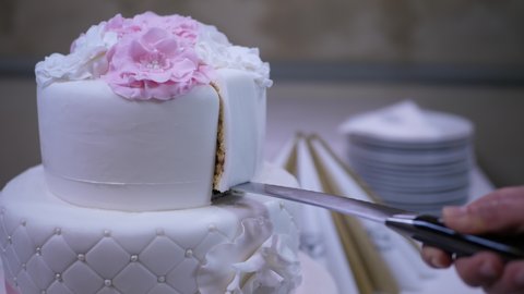 Taking away a slice of a chocolate cake with a knife from the storey cake. Slicing up a white, fondant covered chocolate wedding cake. Close shot with the appetizing confectionery product.