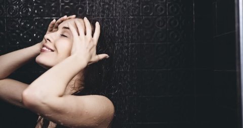 Woman taking shower in slow motion. Filmed in 4K DCi resolution. Young beautiful woman taking a shower and washing her hair, smiling. Beauty and wellbeing concept.