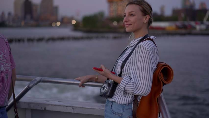Cheerful woman tourist in trendy clothing enjoying getaway time for discover world ride on water sightseeing boat and laughing, happy Caucasian hipster girl with instant camera and cellphone smiling
