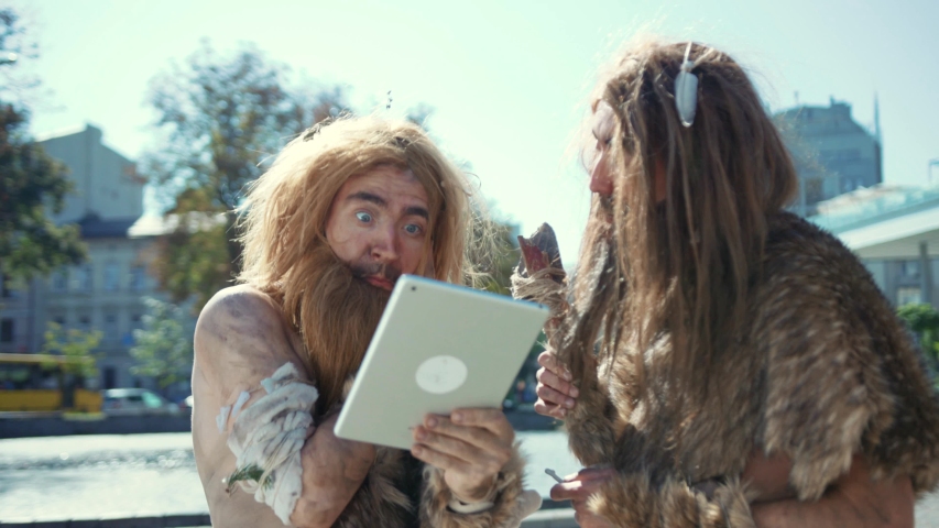 Happy savages in animal fur using modern tablet browsing internet having fun. Hunter-gatherers of ancient tribe in modern times. Evolution. Royalty-Free Stock Footage #1038157211