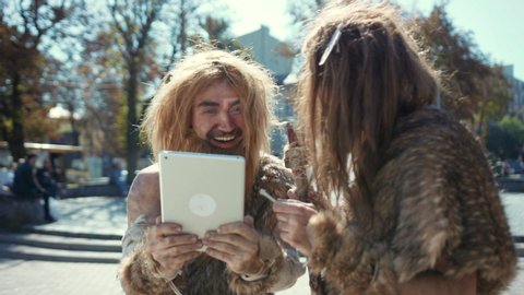 Happy savages in animal fur using modern tablet browsing internet having fun. Hunter-gatherers of ancient tribe in modern times. Evolution.