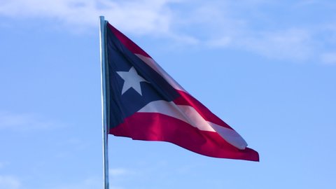 Flag of Puerto Rico waving against a blue sky background in slow motion.