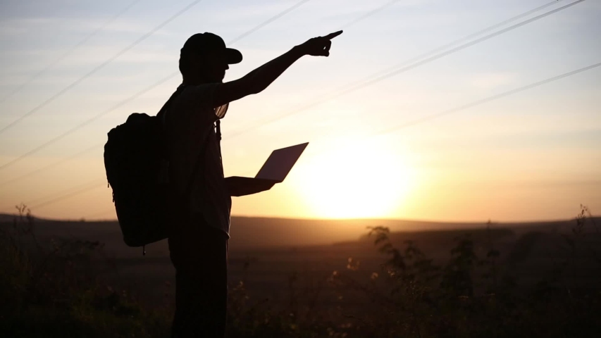 Silhouette of young guy on a hiking, using laptop for searching coordinates.