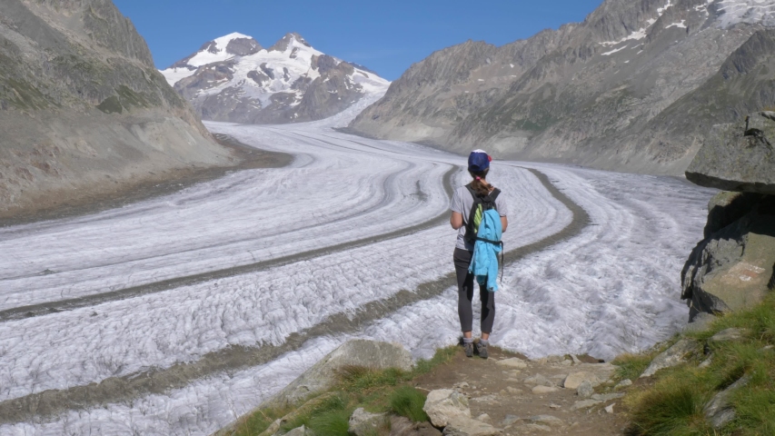 A lone female hiker looks toward a vast glacier. She stops on the trail edge to stop and look in awe at the vast mountains and glacier that surround her.