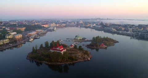 Helsinki south harbor, Aerial, tracking, drone shot, panning around the valkosaari and luoto islands and the cityscape, colorful sky, at sunrise, on a foggy dawn, in Helsingfors, Uusimaa, Finland