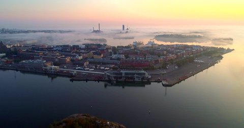 Helsinki foggy morning, Aerial, tracking, drone shot, katajanokka cityscape, colorful sky and fog clouds, over the tervasaari island and the sea, at sunrise, on a sunny and misty autumn dawn, in