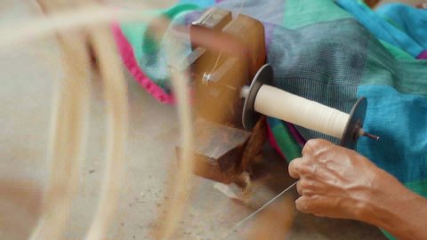 A white cotton thread winding on a spool guided by a hand-loom weaver for textile production