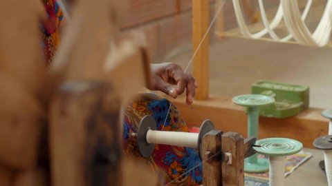 A white cotton thread winding on a spool guided by a hand-loom weaver for textile production