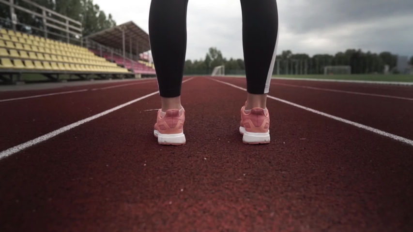 young woman is preparing for the run in the stadium. she is putting her shoelace inside the shoes.