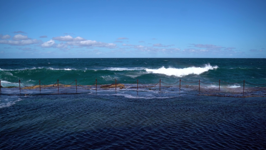 Large blue pacific ocean waves crashing into shoreline rocks on coast to beach on windy summers day