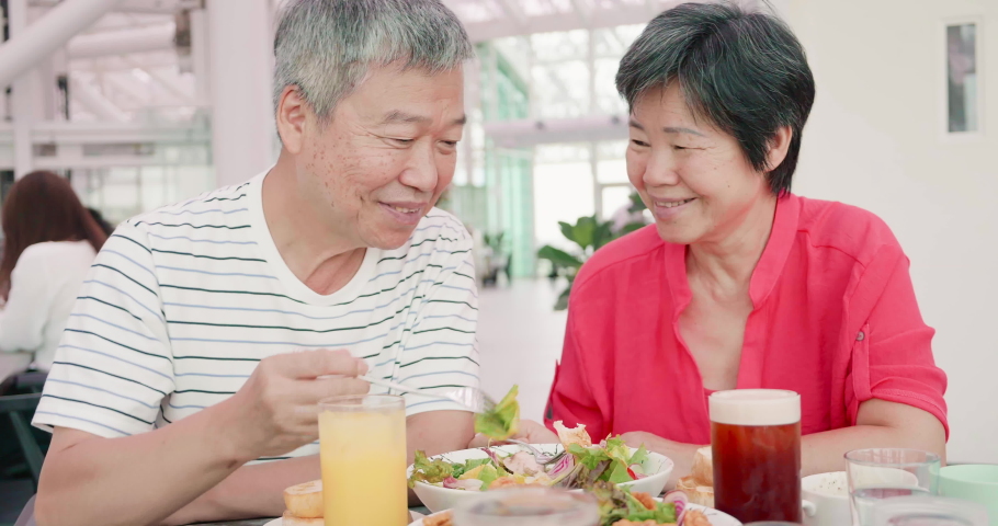 asian elder couple is eating in the restaurant and share their food to each other