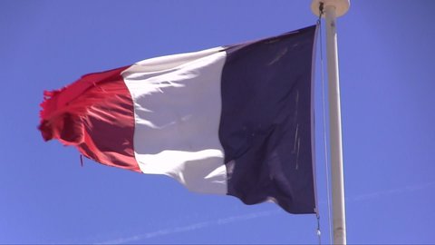 French flag waving in strong breeze against blue sky