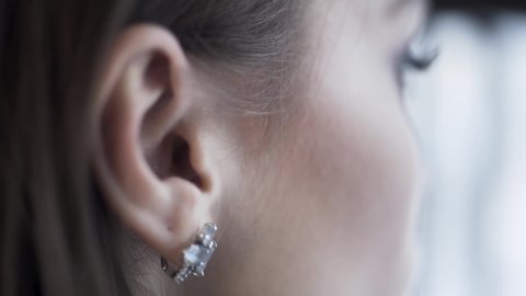 Close up of brunette woman hand pushing her hair back behind her ear and baring a silver earring. Action. Side view of a girl face touching her dark hair.