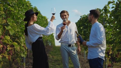 Wealthy couple tasting red wine with professional sommelier pouring drink into glasses. Private degustation on vineyard.