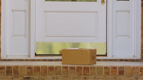 Man opening front door and picking up package delivered to the doorstep. Retrieving shipment parcel box from porch of house.