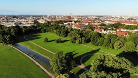Aerial drone video of Englischer Garten and Munich city skyline. Sunny summer morning, clear blue sky