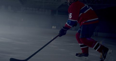 Hockey player skating in dramatically lit hockey rink skating and stick handling then taking a slap shot and scoring a goal as seen from behind hockey net