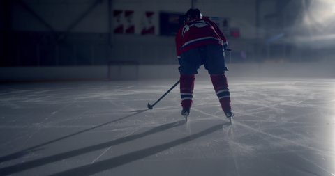 Close up of hockey player skating in dramatically lit hockey rink skating and stick handling then taking a slap shot and scoring a goal 