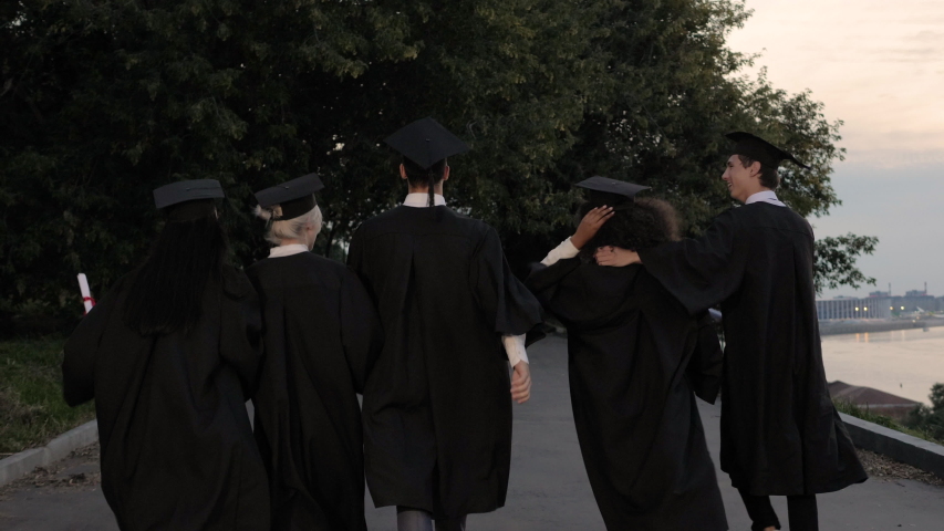 Five young graduates jump up while walking.