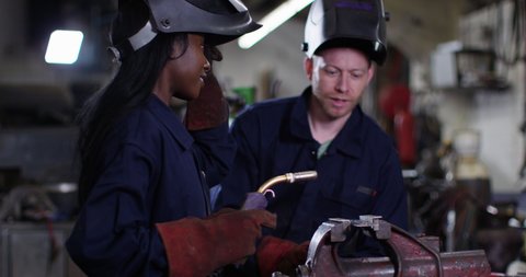 4K Experienced metalworker training female apprentice in industrial workshop