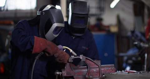 4K Male & female mechanics welding metal parts in workshop & smiling