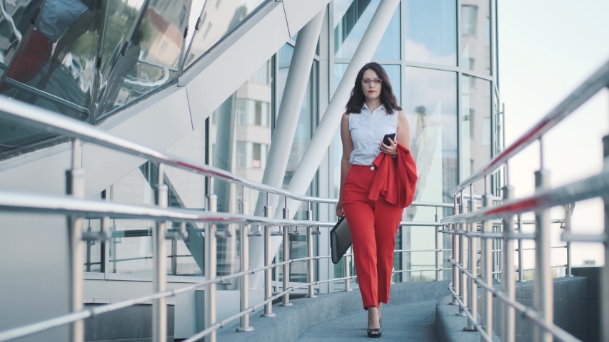Confident business woman in a formal suit walks against the background of a modern business center