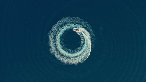 Aerial shot of a fast speedboat with a red roof top going around in the circle in a clear turquoise magical ocean. Top travel destination. 4K.