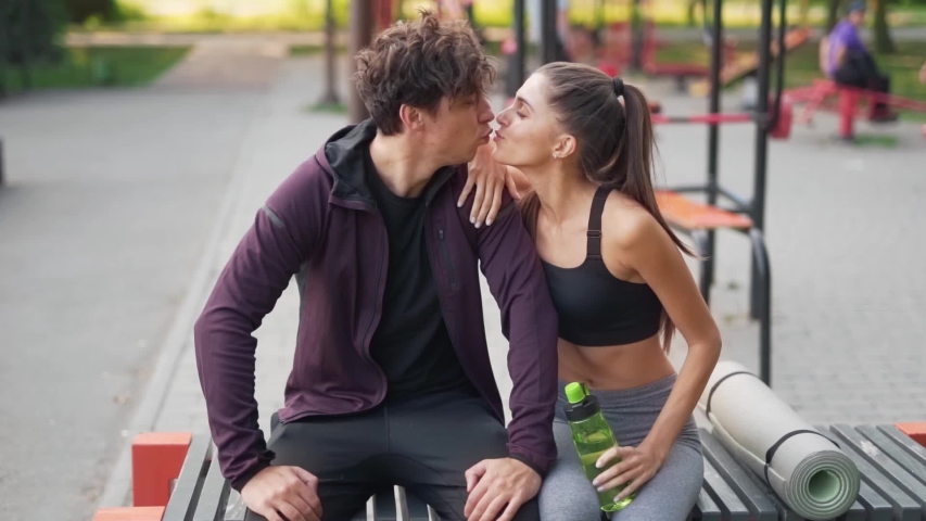 Young Athletic Couple Cuddling On A Bench Seat Outdoors