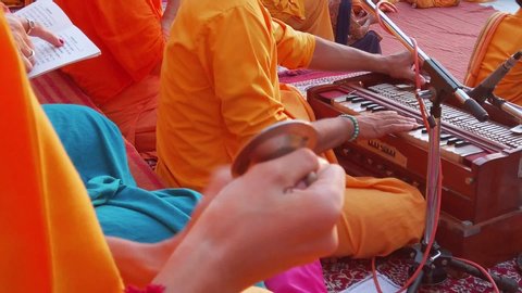 Rishikesh, India - Circa September 2019. Slow motion view of Ganga Aarti ceremony in Parmarth Niketan ashram. Monk plays hand-pumped harmonium and other one plays brass thalam in blurred foreground.