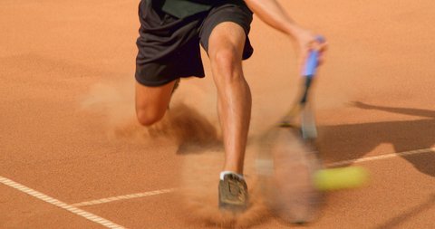 A Tennis Player slides across a clay tennis court and plays the shot in slow motion.