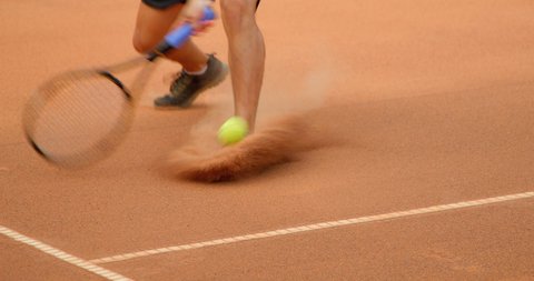 A tennis player slides across a clay tennis court in slow motion and plays the shot.